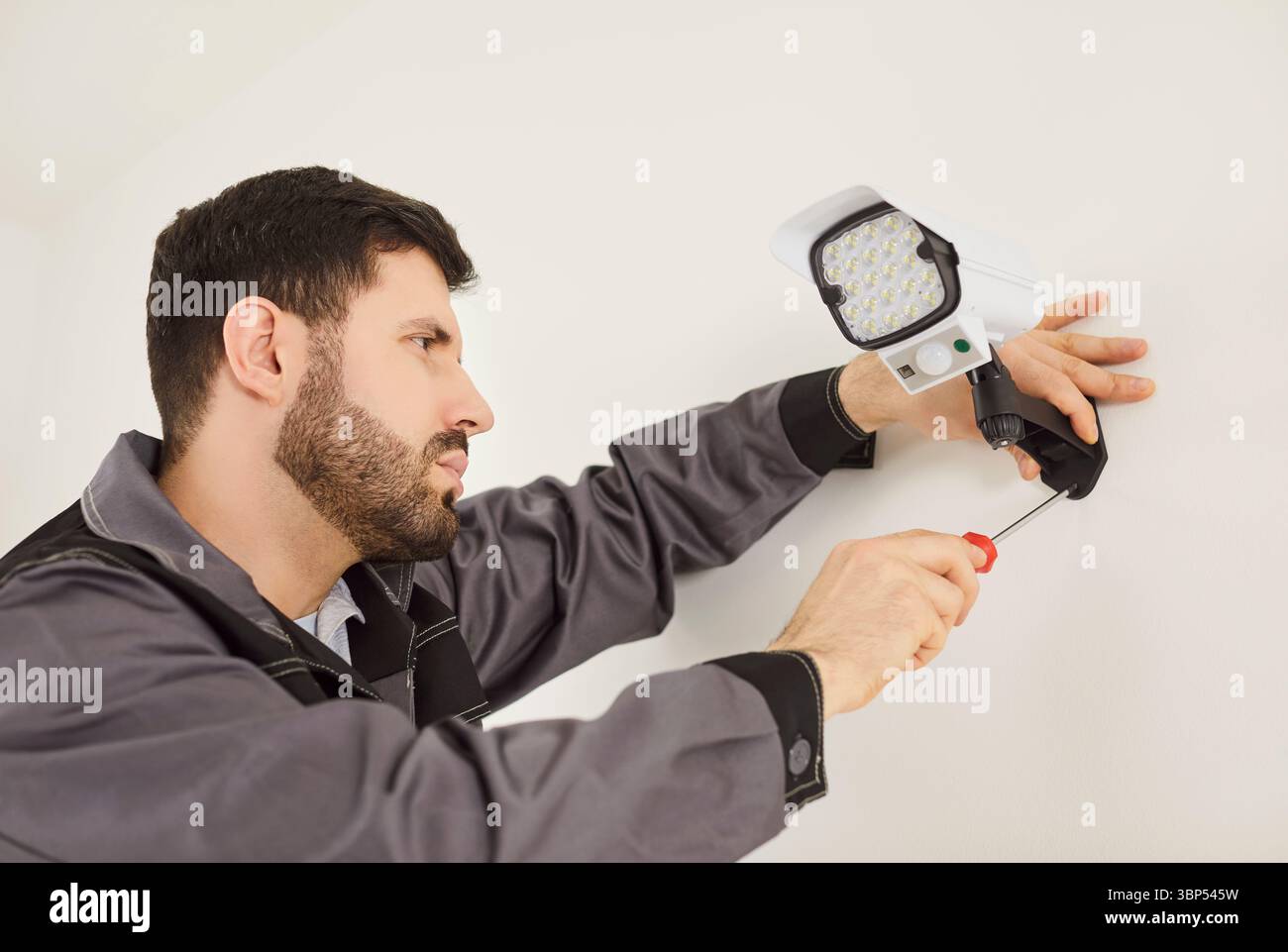 Professional handyman using screwdriver for setting up security camera on white wall Stock Photo