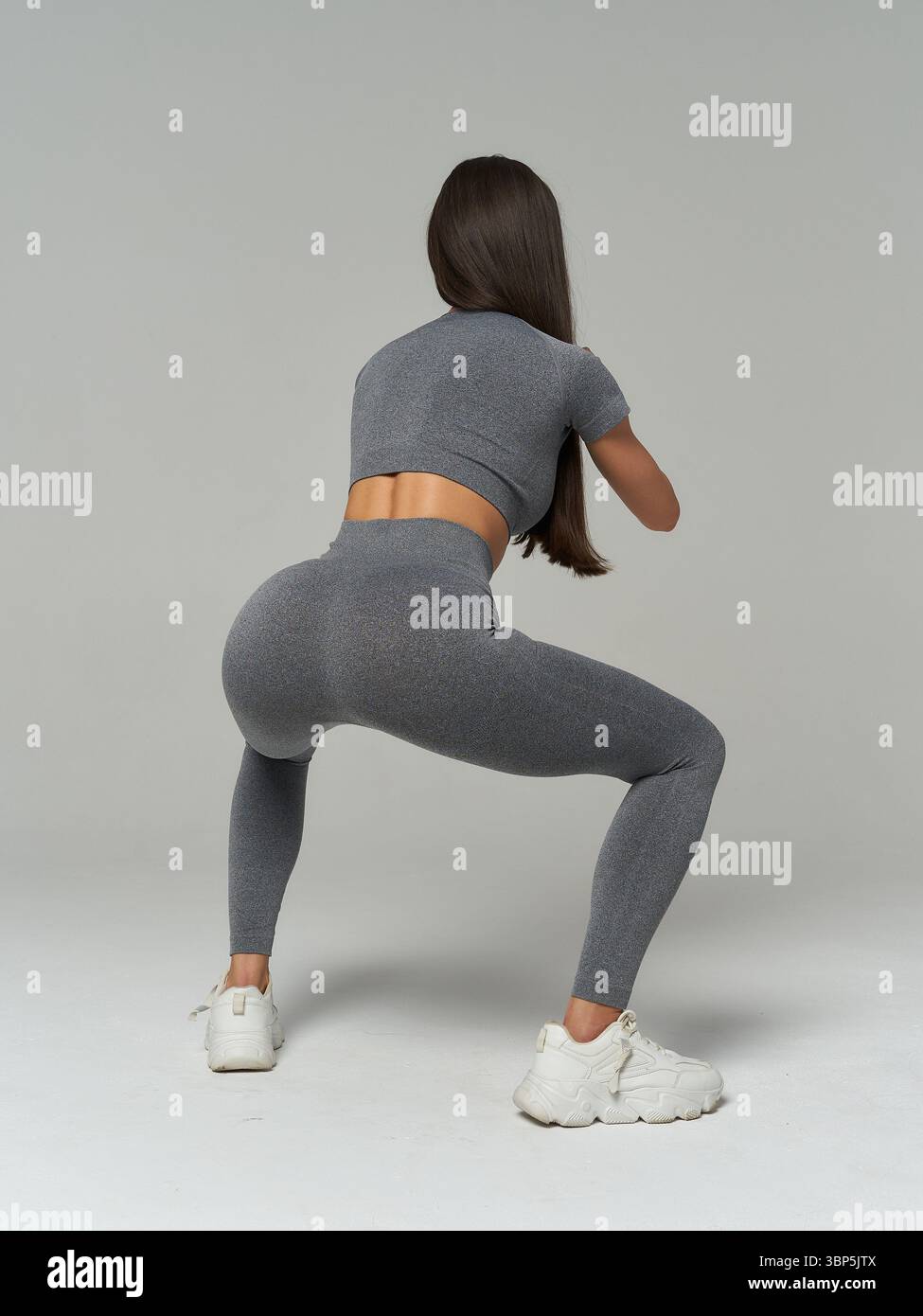 Athletic woman in gray activewear performing squat from behind ...