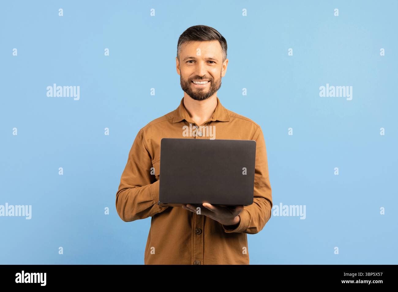 Confident young man smiling and holding laptop in hands Stock Photo