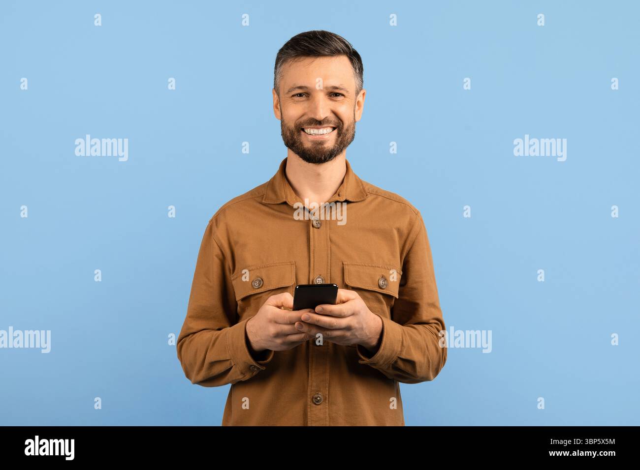 Smiling young man using smartphone and looking at camera Stock Photo