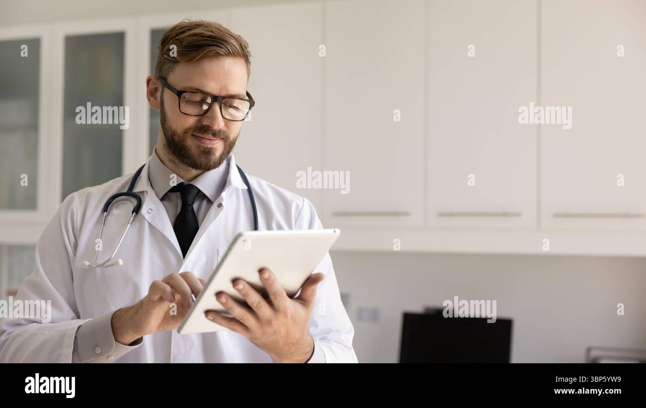 Focused positive young doctor man using digital tablet Stock Photo