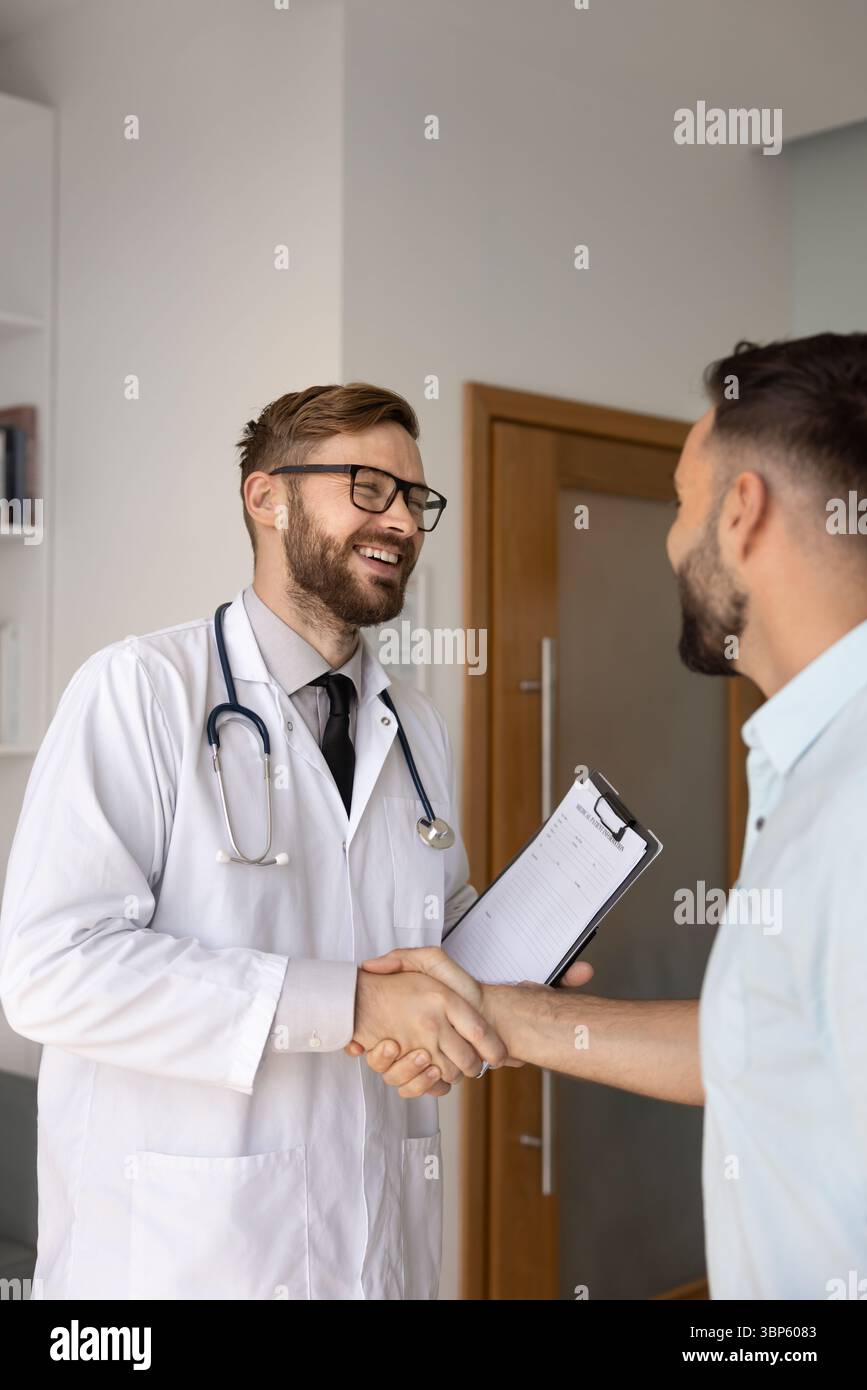Positive young Caucasian doctor man shaking hands with patient, Stock Photo
