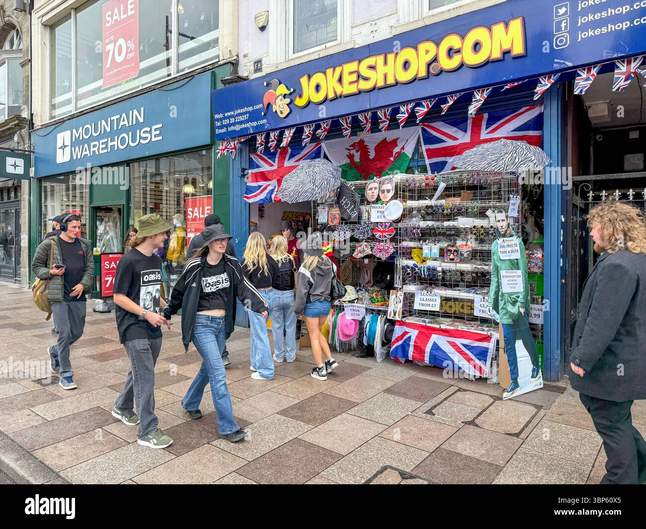 Oasis Tour Cardiff Concert Fans Wearing Band T-Shirts and Merchandise Outside Jokeshop - Smartphone Captured Stock Image