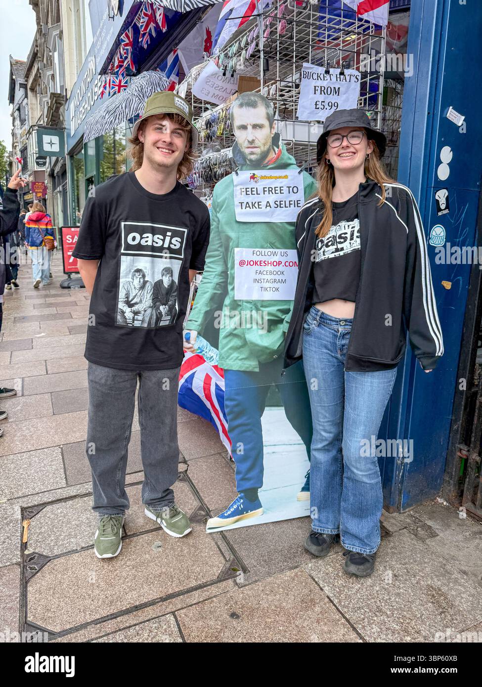 Oasis Tour Cardiff Concert Fans Wearing Band T-Shirts and Merchandise Outside Jokeshop - Smartphone Captured Stock Image
