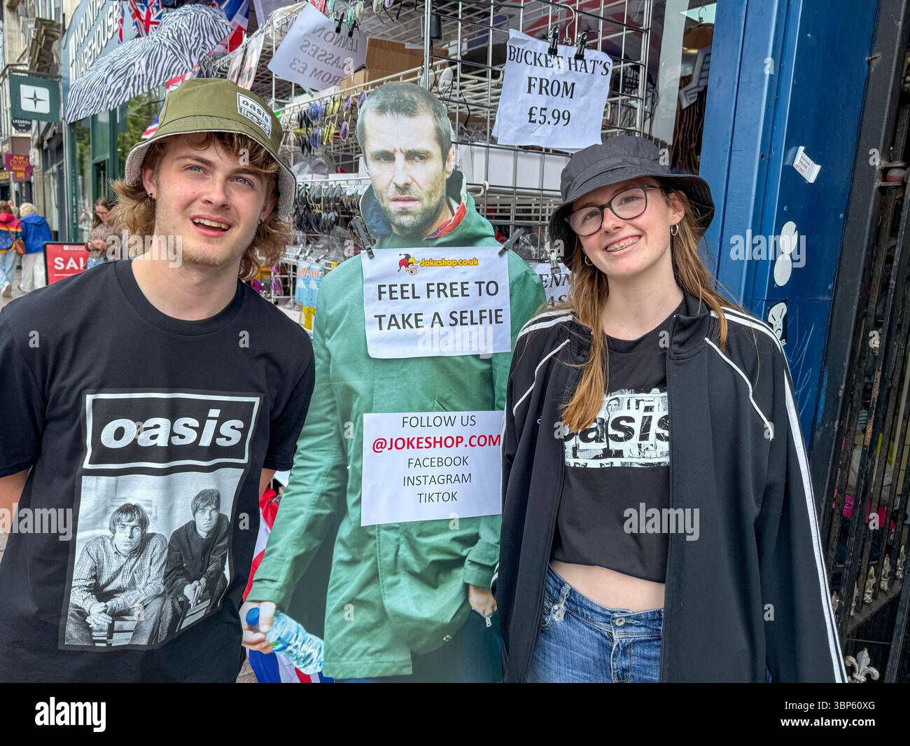 Oasis Tour Cardiff Concert Fans Wearing Band T-Shirts and Merchandise Outside Jokeshop - Smartphone Captured Stock Image