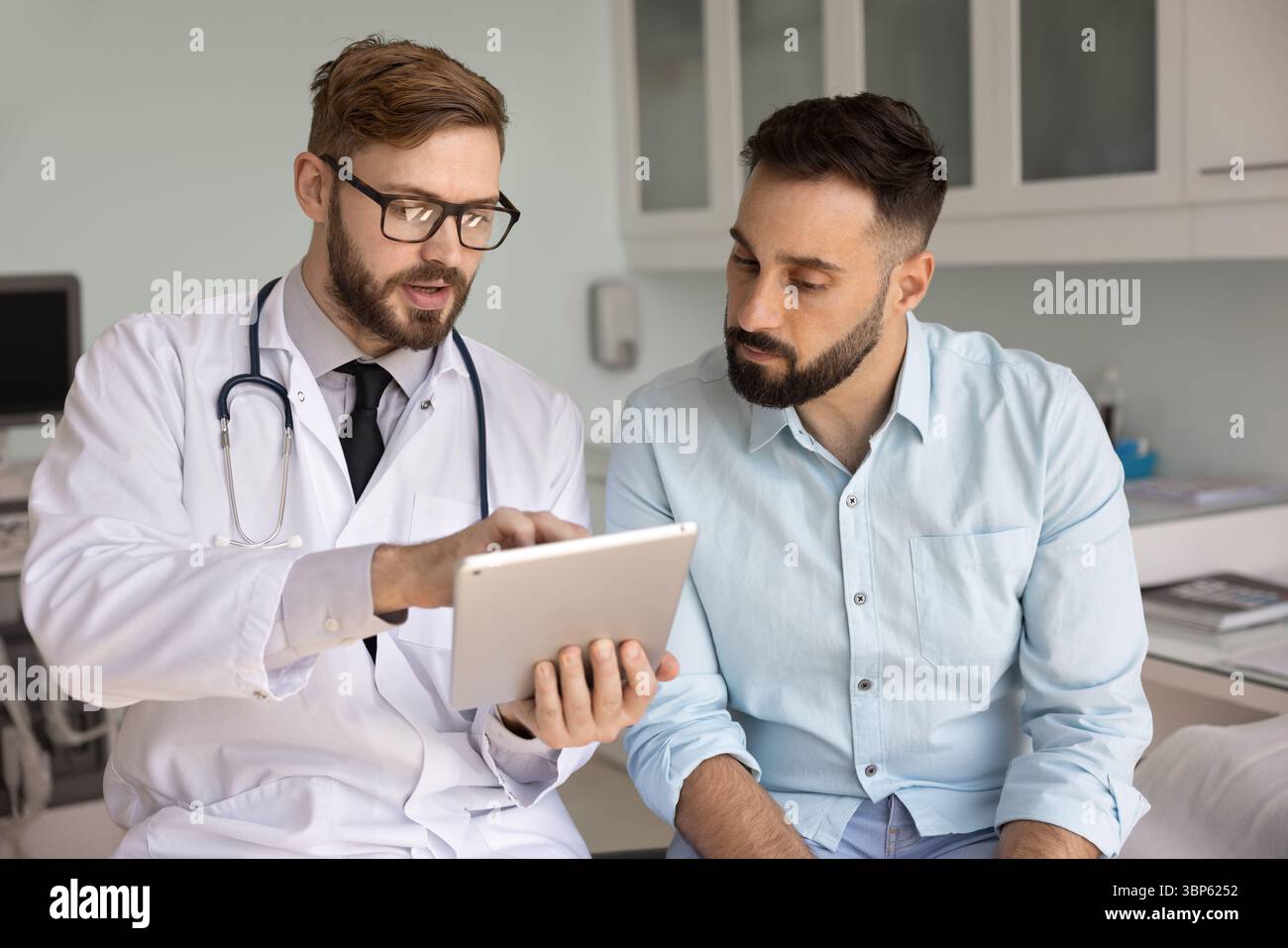 Serious doctor in glasses explaining electronic prescription to Latin man Stock Photo