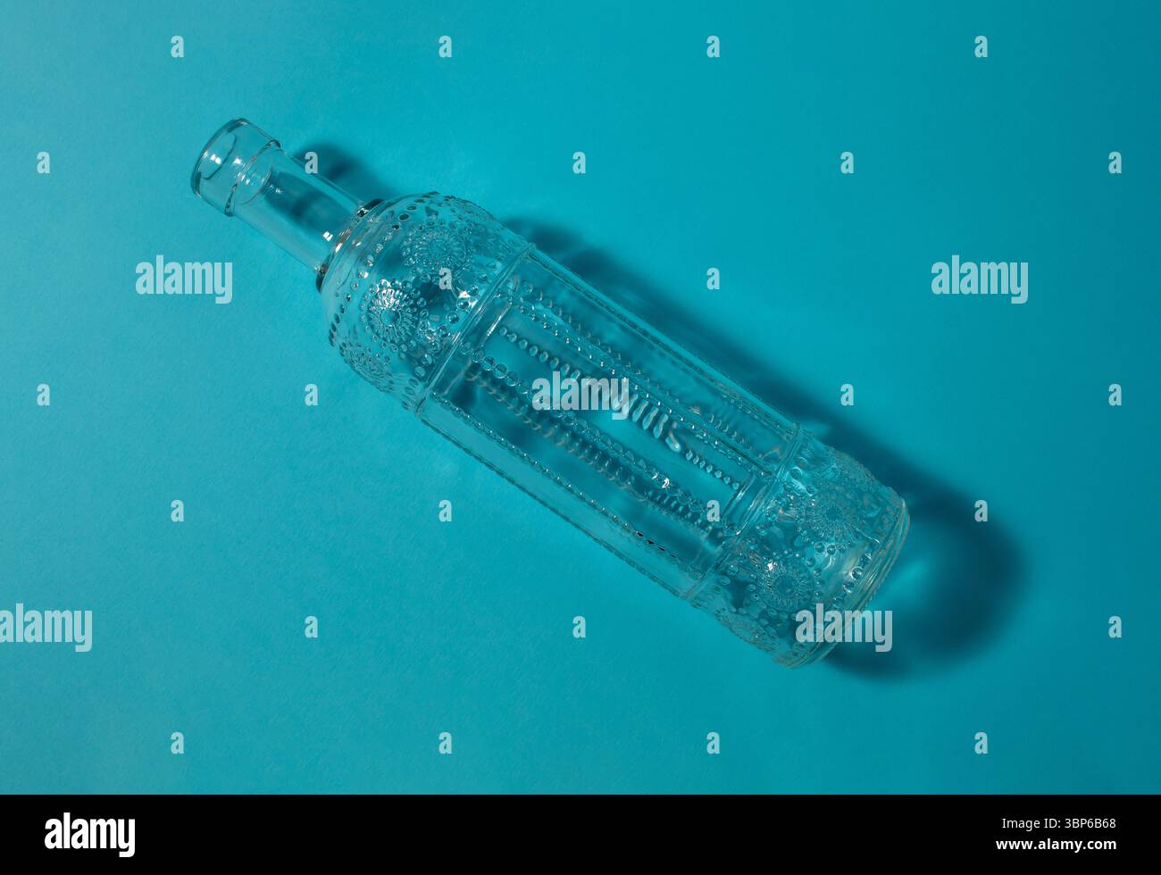 Glass bottle with embossed design on a blue background. Stock Photo