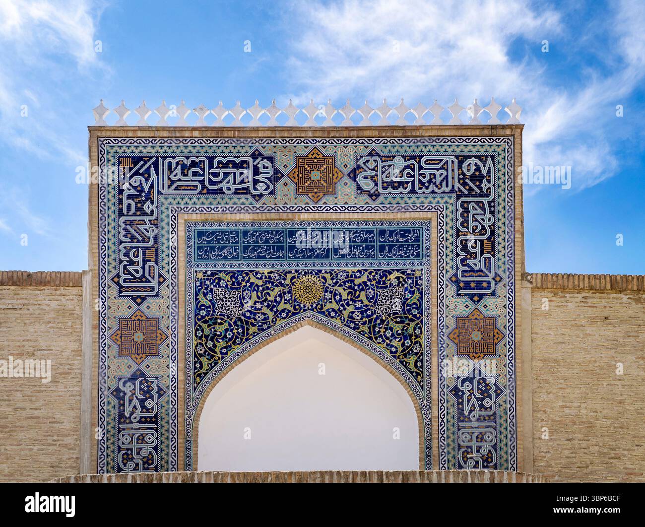 A stunning architectural detail featuring intricate blue tile work and Arabic calligraphy on a grand archway against a bright blue sky. Stock Photo