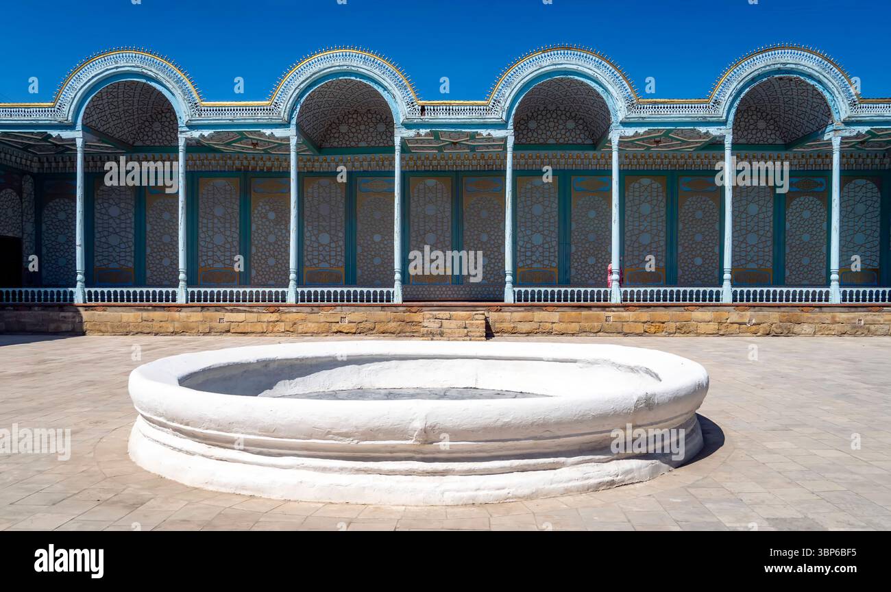 A traditional architectural courtyard featuring a circular white fountain surrounded by intricately designed arches and walls with colorful patterns. Stock Photo