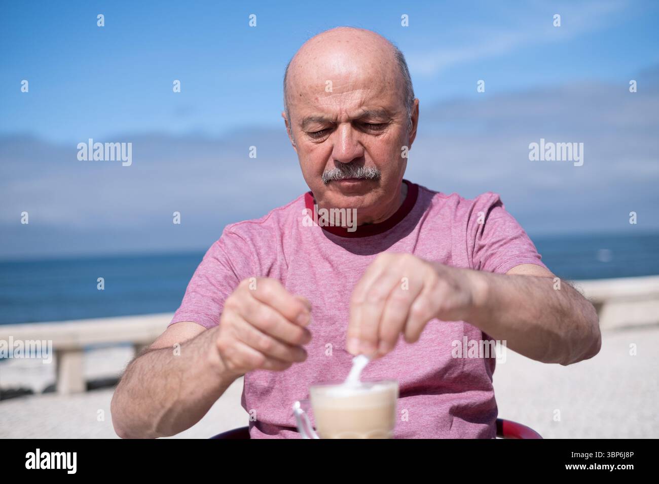 Elderly Man Adding a Lot of Sugar to Coffee While Sitting on a Summer Terrace Stock Photo