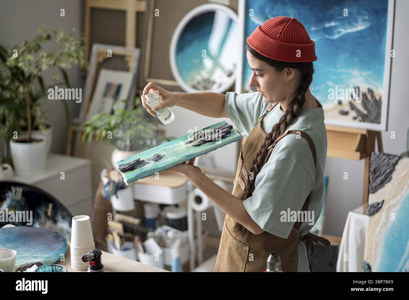 Image showcasing Focused woman working on epoxy painting, spraying canvas with special ...