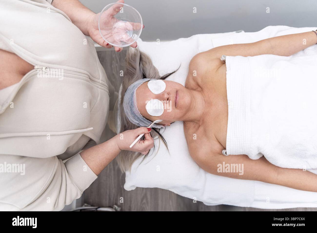Beautician applying a nourishing face treatment to a client relaxing on a massage table in a tranquil spa environment Stock Photo
