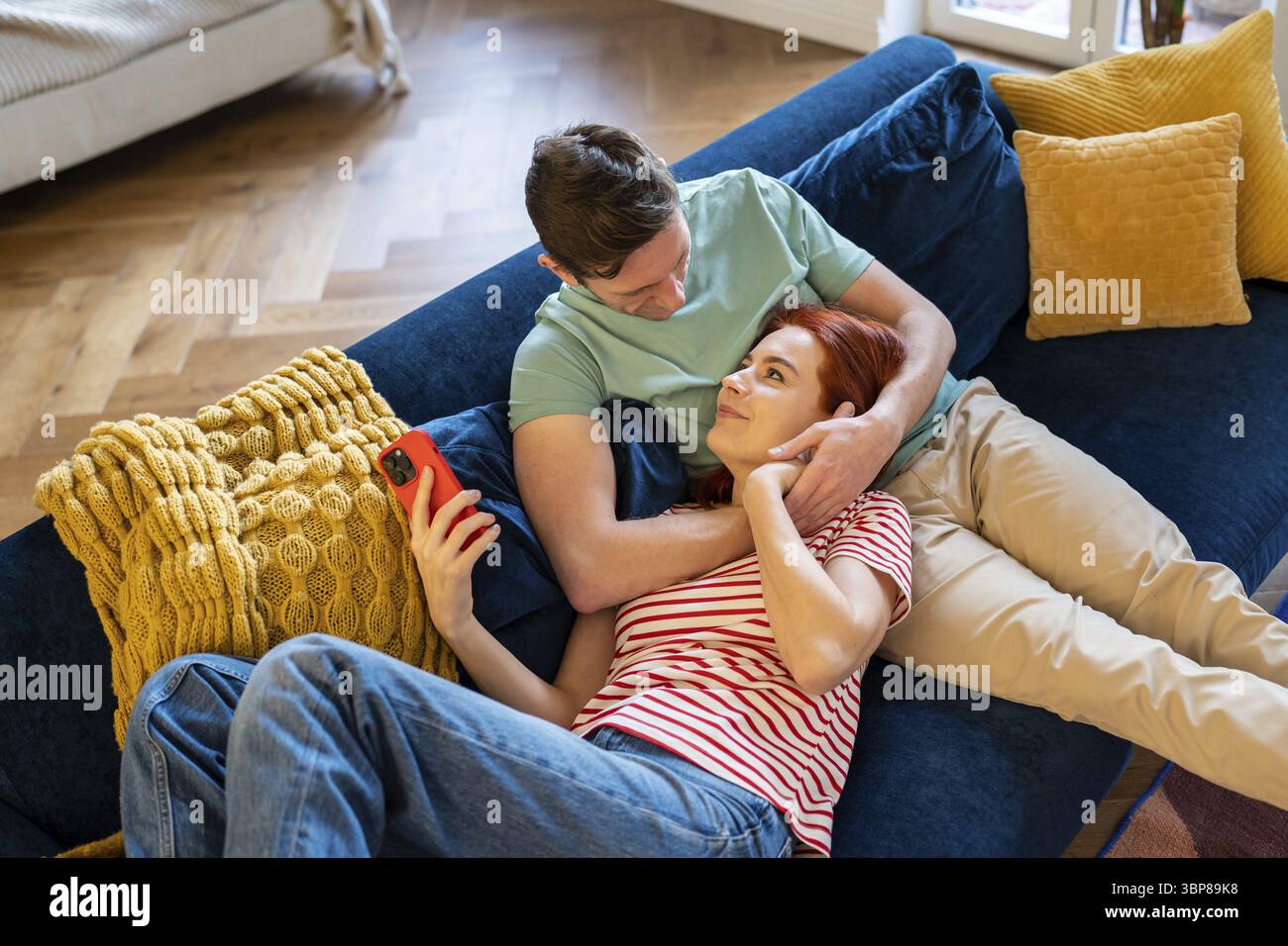 Caring man gentle hug wife enjoying leisure time together, resting on sofa. Smiling woman lying on loving husband laps at home. Romantic relationship. Stock Photo