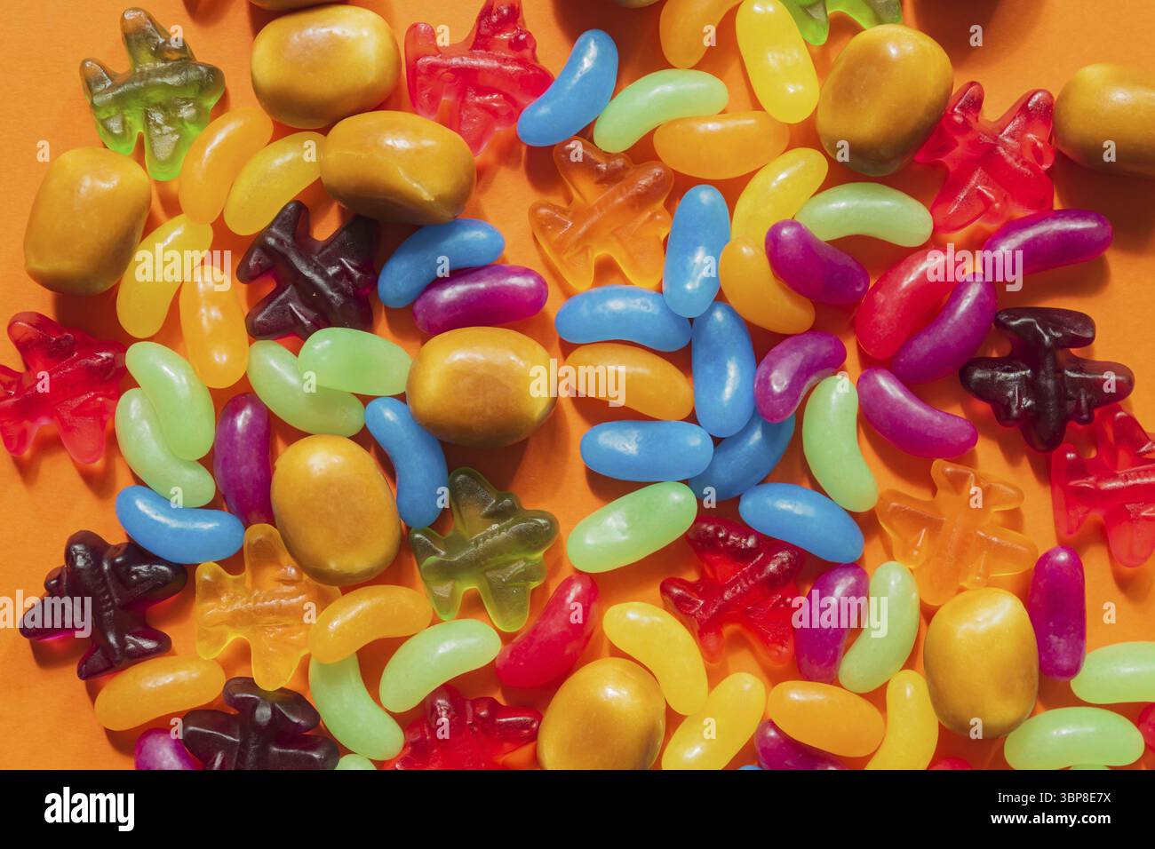 Multi-colored glazed jelly beans sweets on orange paper background Stock Photo