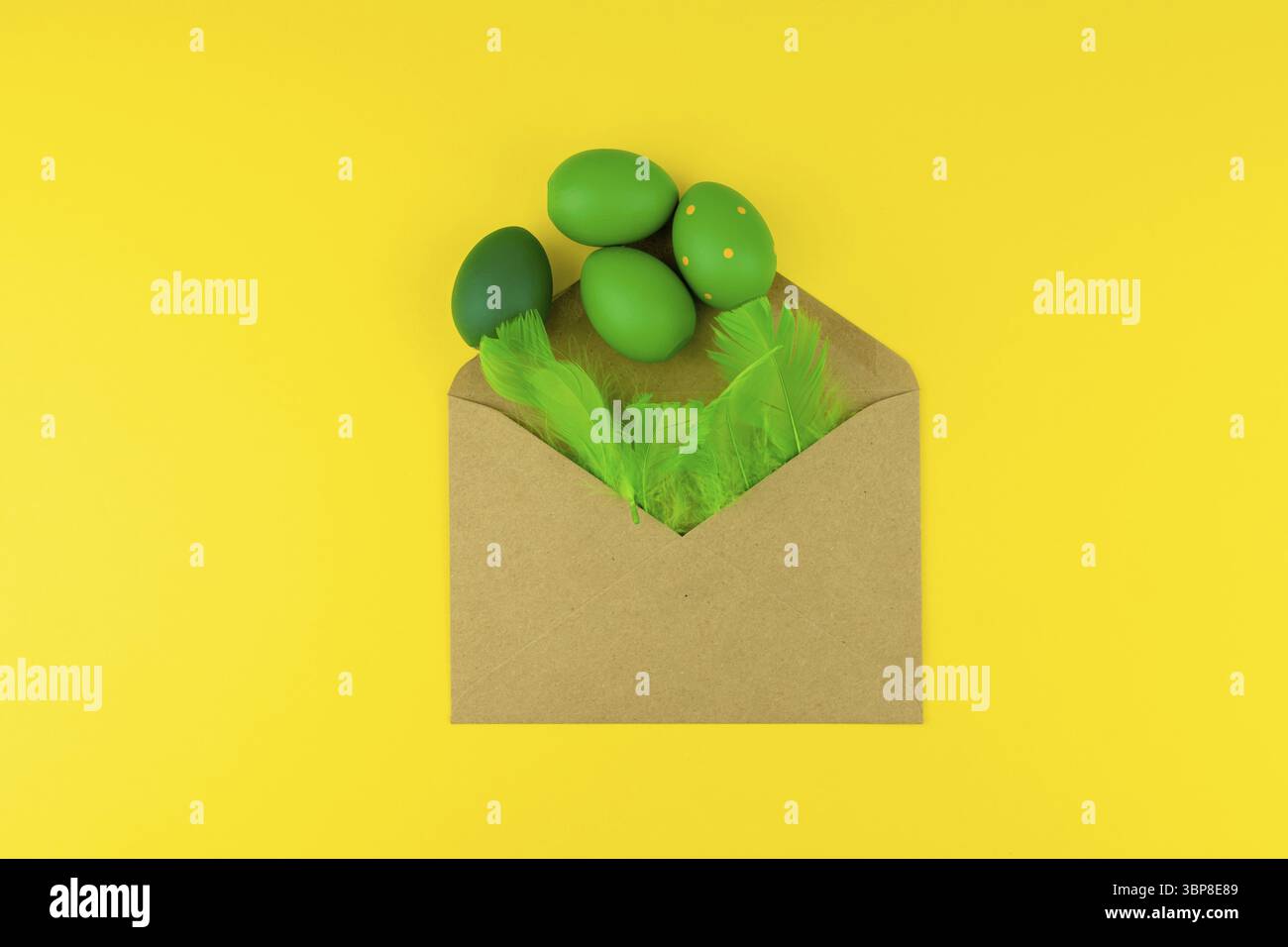 Spring Easter layout with green feathers and eggs, craft envelope on yellow background. Copy space for text for text Stock Photo