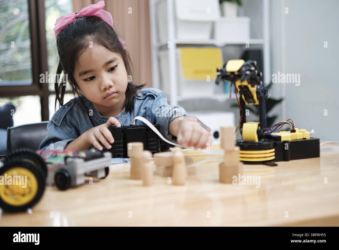 A primary school girl focuses on operating a robotic arm with a remote control, demonstrating STEM education in action Stock Photo