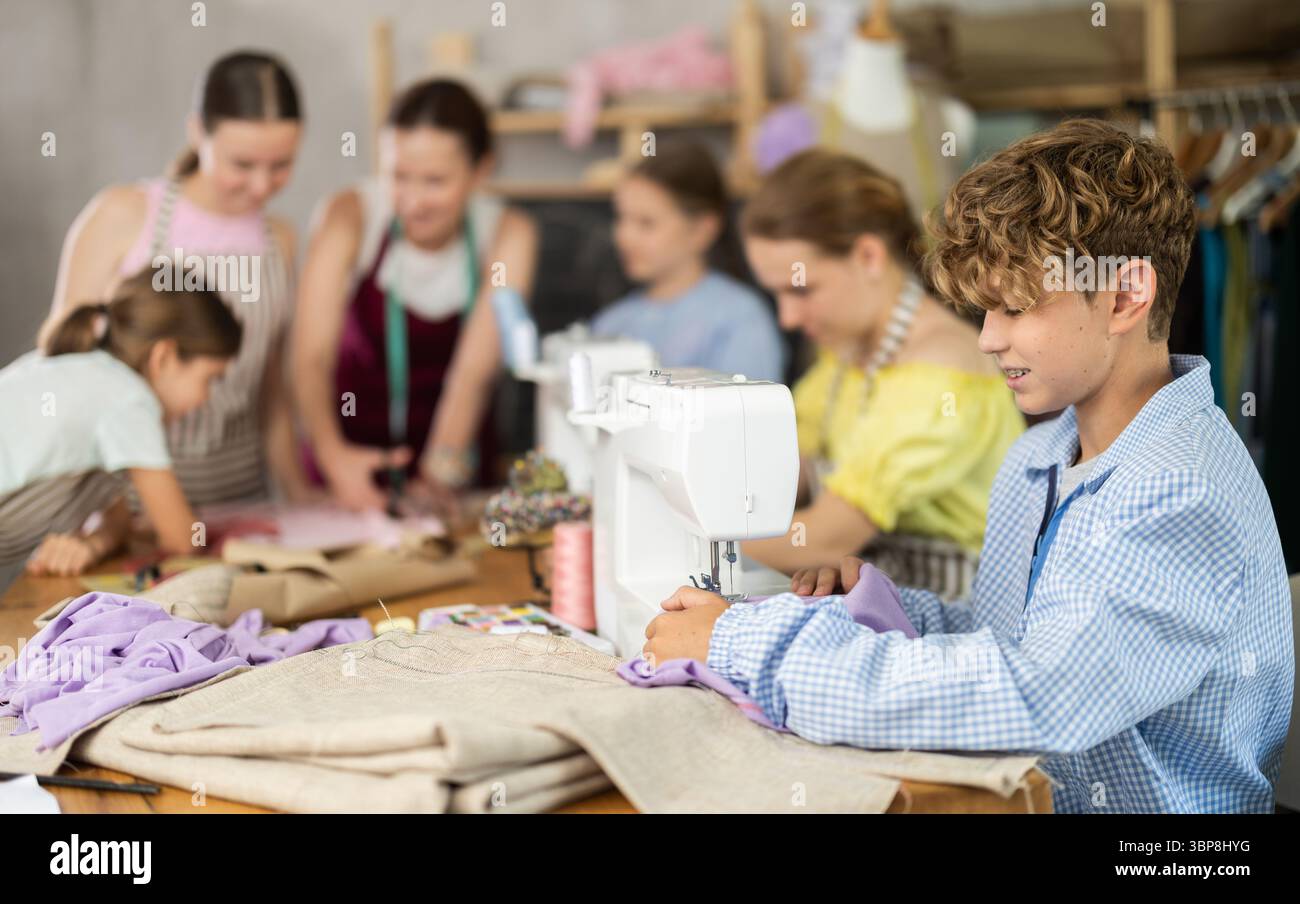 Boy learns to sew on sewing machine in class as children watch him ...