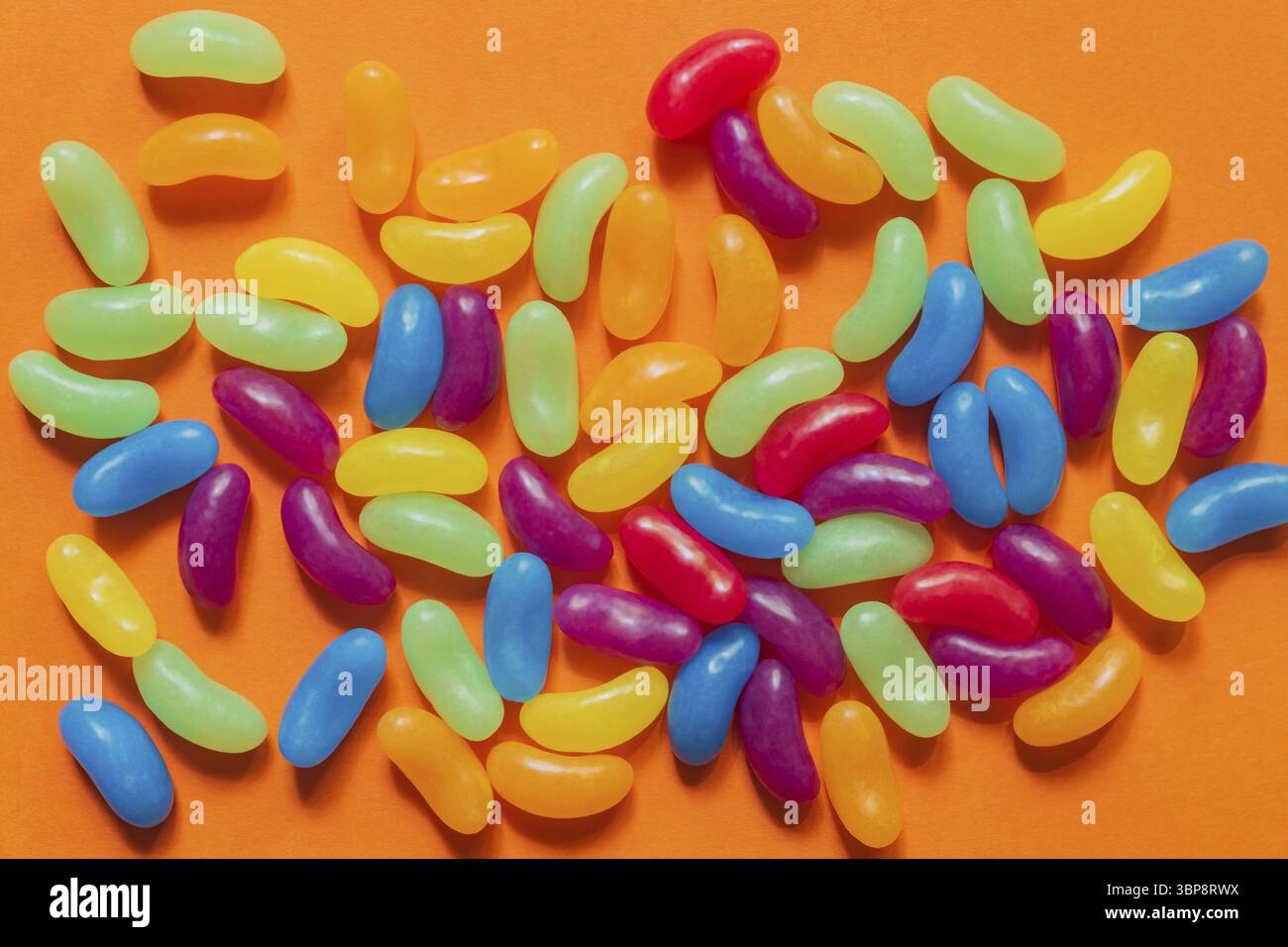 Multi-colored glazed jelly beans sweets on orange paper background Stock Photo
