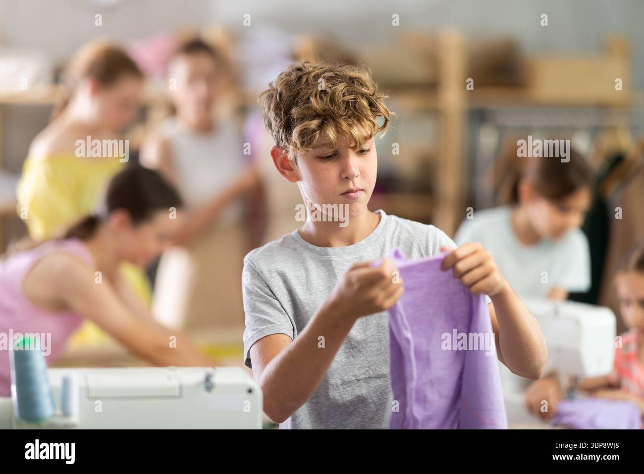 Boy checking stitched fabric at school sewing workshop Stock Photo