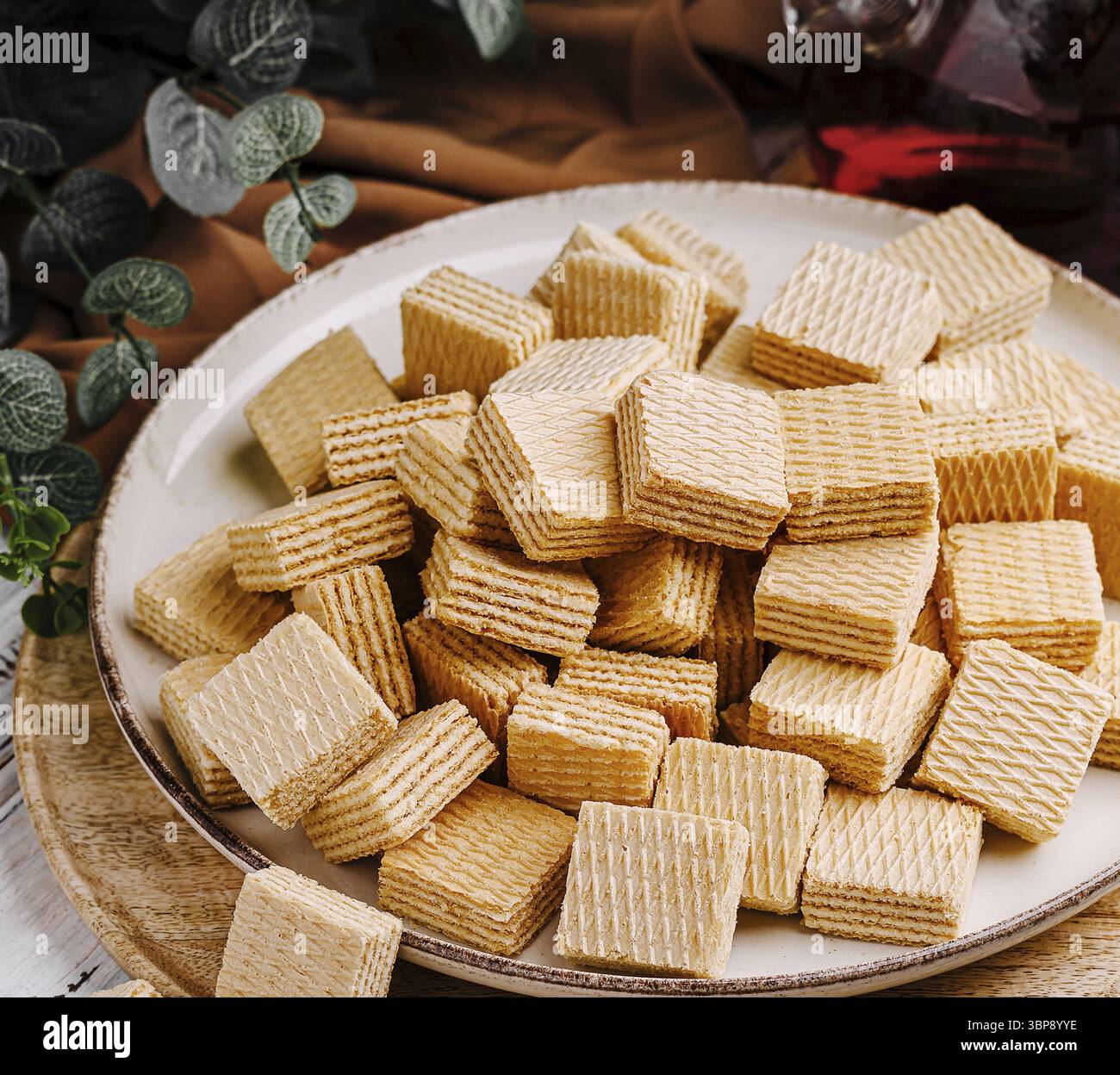 Food, A plate is filled with neatly stacked wafers in a cozy setting. The wafers are golden-brown and have a textured surface, surrounded by soft fabr Stock Photo