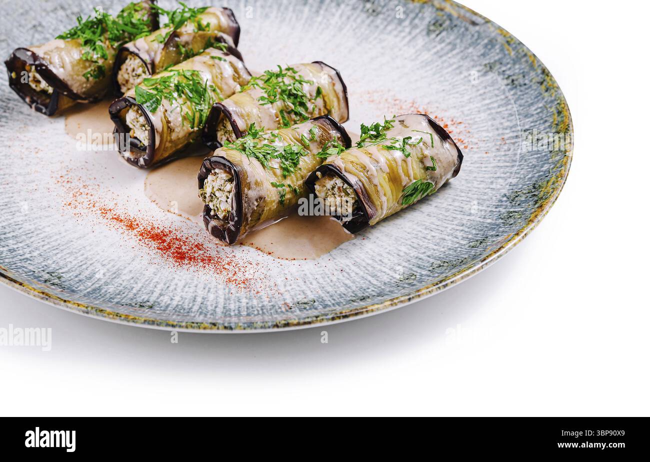 Food, Delicious eggplant rolls stuffed with nuts and herbs are lying on the plate decorated with sauce and spices Stock Photo