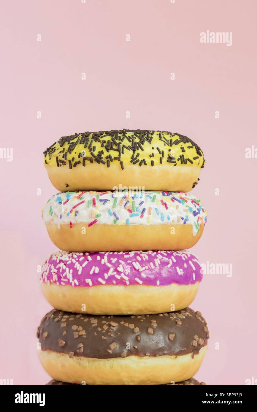 Stack of glazed sweet doughnuts with sprinkles and nuts on pink background. Copy pace for your text Stock Photo