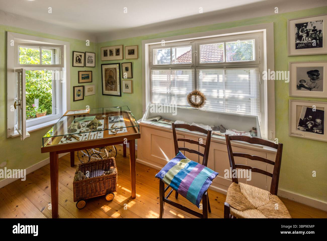 The ground floor of the Mia and Hermann Hesse House in Gaienhofen, Baden-Württemberg, Germany, displays personal items and photographs by photographer Mia Hesse in a glass case. A wicker pram and framed pictures complete the exhibition by the window seat. Stock Photo