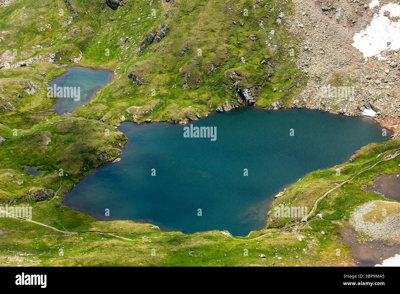 capra lake of fagaras ridge in summer. transylvania alps. rippled water surface and grass on the shore view from above. alpine pond carpathian mountai Stock Photo