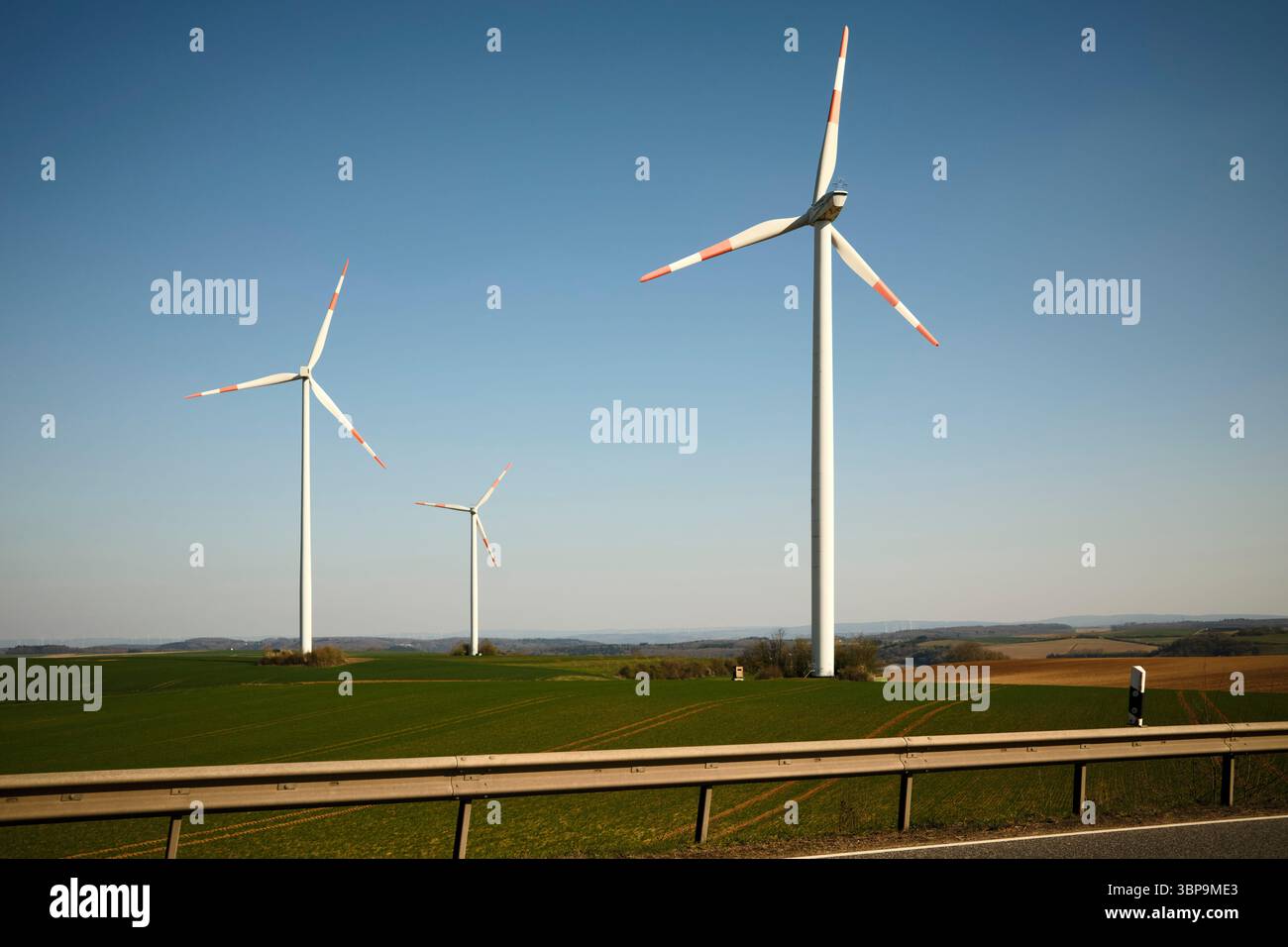 Wind turbines stand tall against a clear blue sky in a sprawling green ...