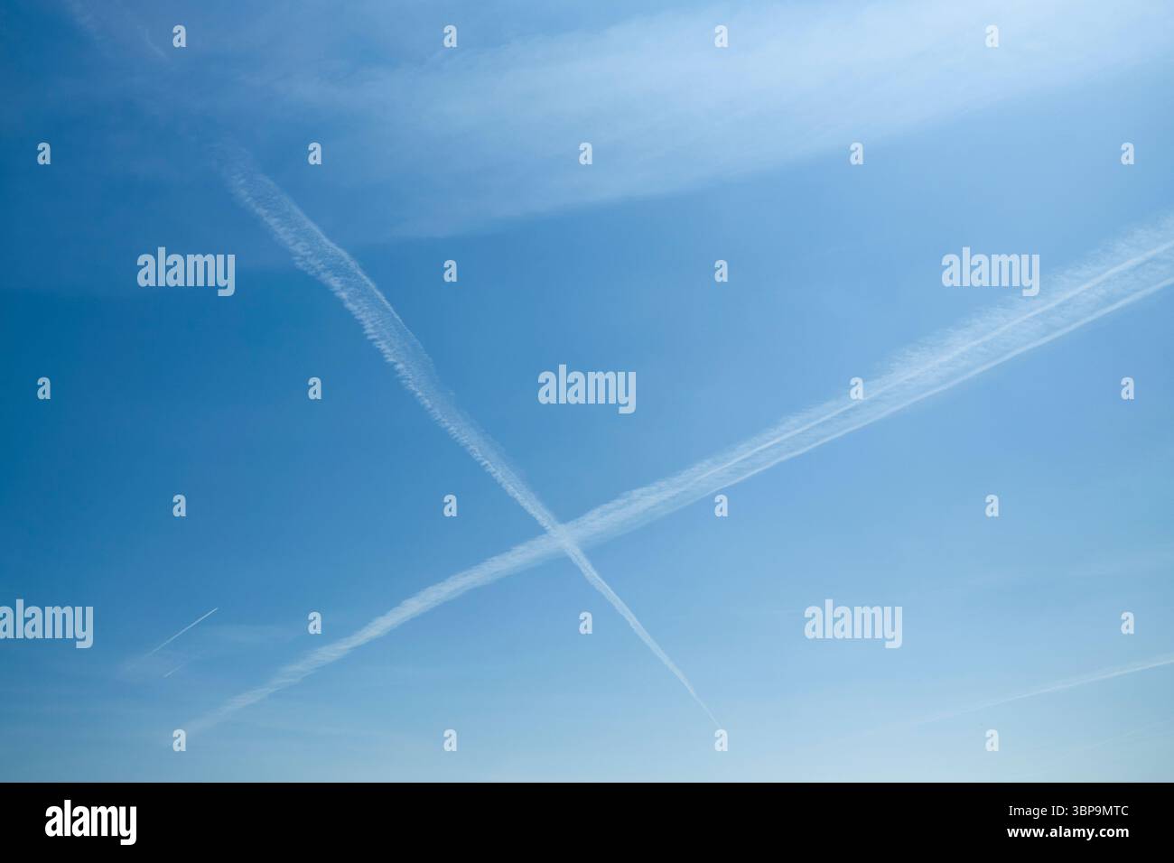 Clear blue sky with intersecting airplane contrails forming an X shape ...