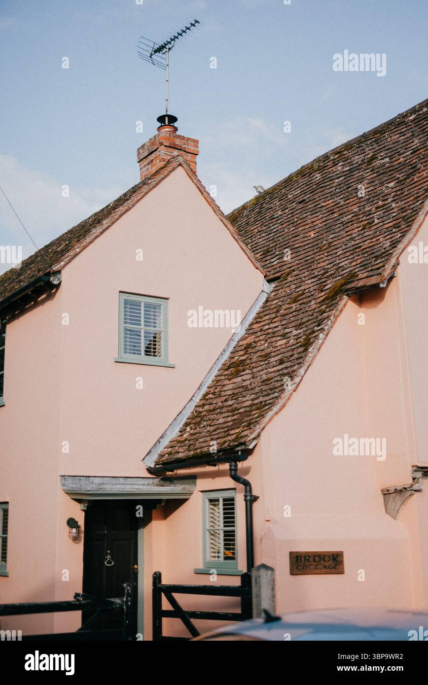 A house with a pink exterior and a black front door. The house has a chimney and a satellite dish on top. The house is located in a residential area Stock Photo