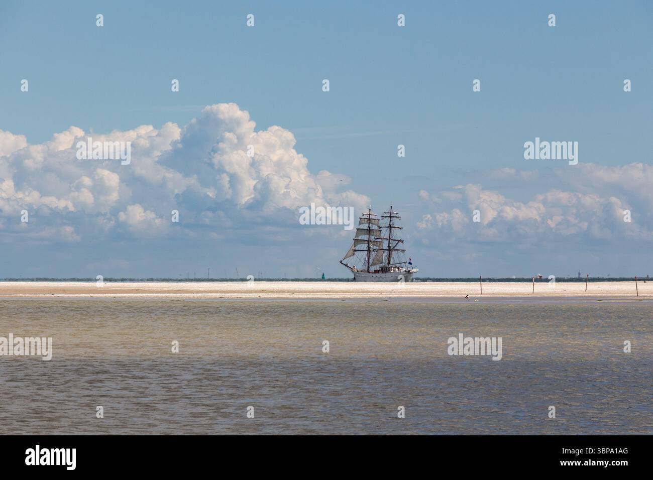 A two masted sailing ship on the horizon against a cloudy blue sky,with ...