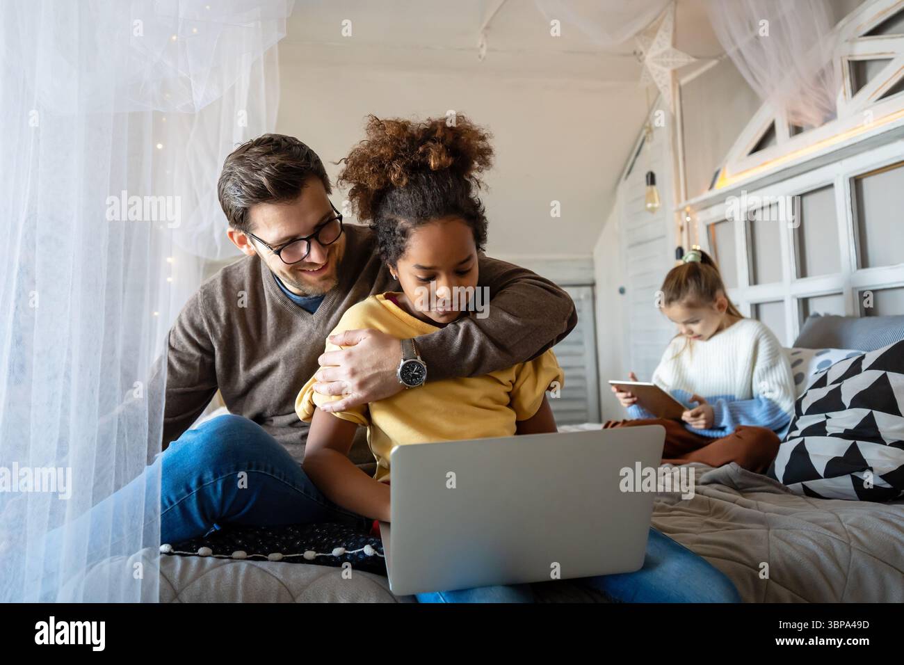 Excited single father plays with diverse, multi-ethnic daughters. Using digital tablet enjoy weekend Stock Photo