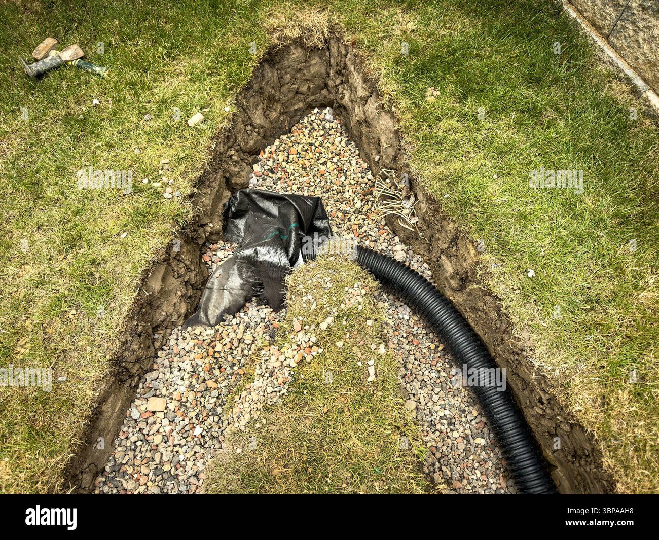 Pipe laying & trenching work in progress on a grassy lawn for field drain drainage installation and landscaping project new build housing problems - Smartphone Captured Stock Image