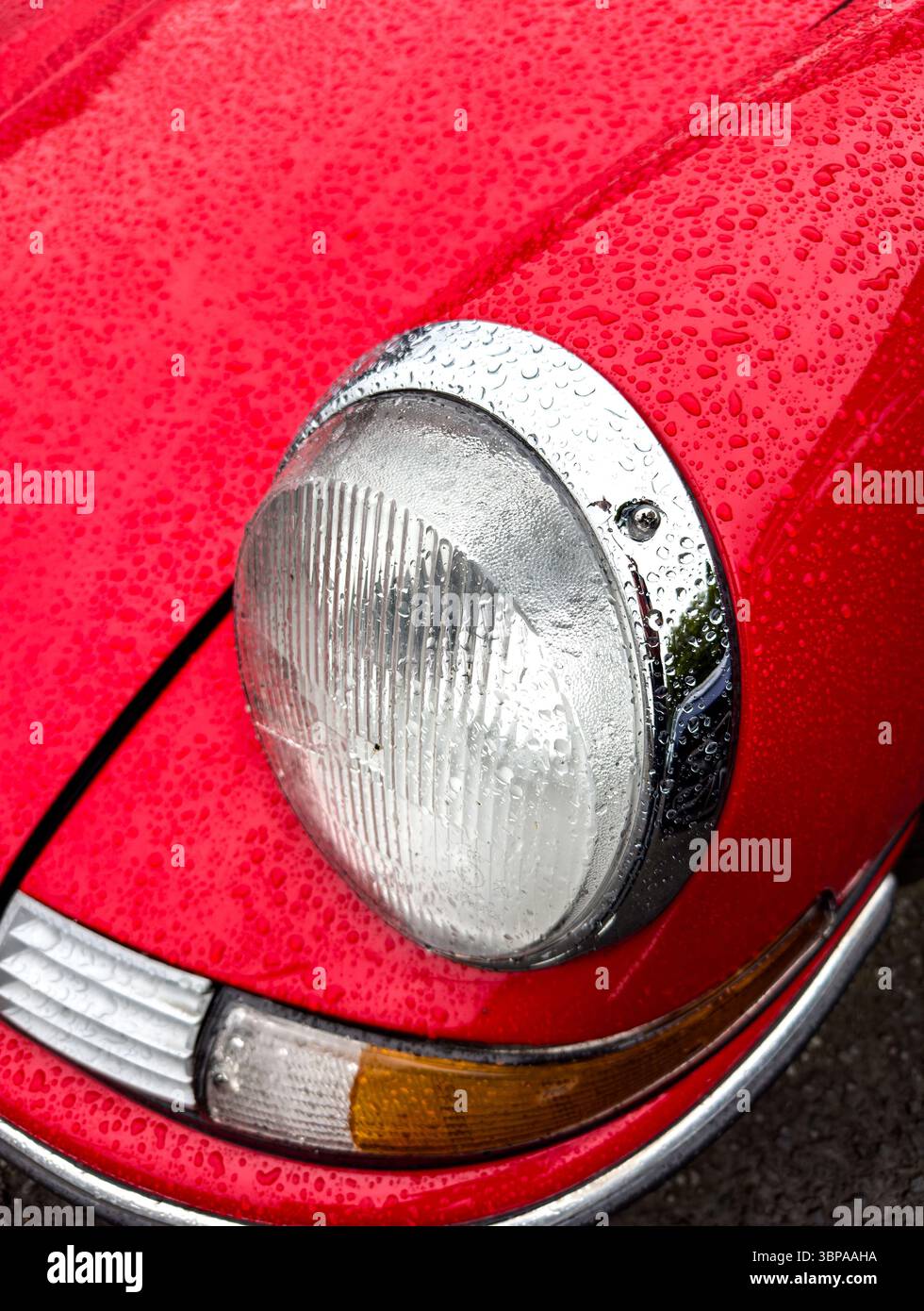 Close-up view of a classic red Porsche 911 sports car front with raindrops highlighting its iconic design and vintage headlights - Smartphone Captured Stock Image