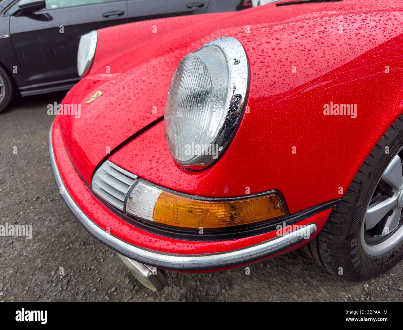 Close-up view of a classic red Porsche 911 sports car front with raindrops highlighting its iconic design and vintage headlights - Smartphone Captured Stock Image