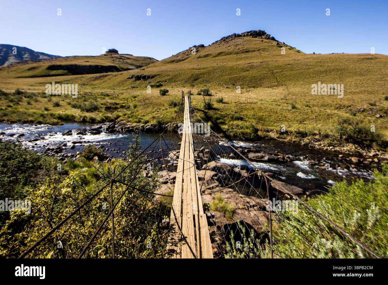 A simple rope bridge crossing a river in the high Afromontane grasslands of the Drakensberg Mountains in South Africa. Stock Photo