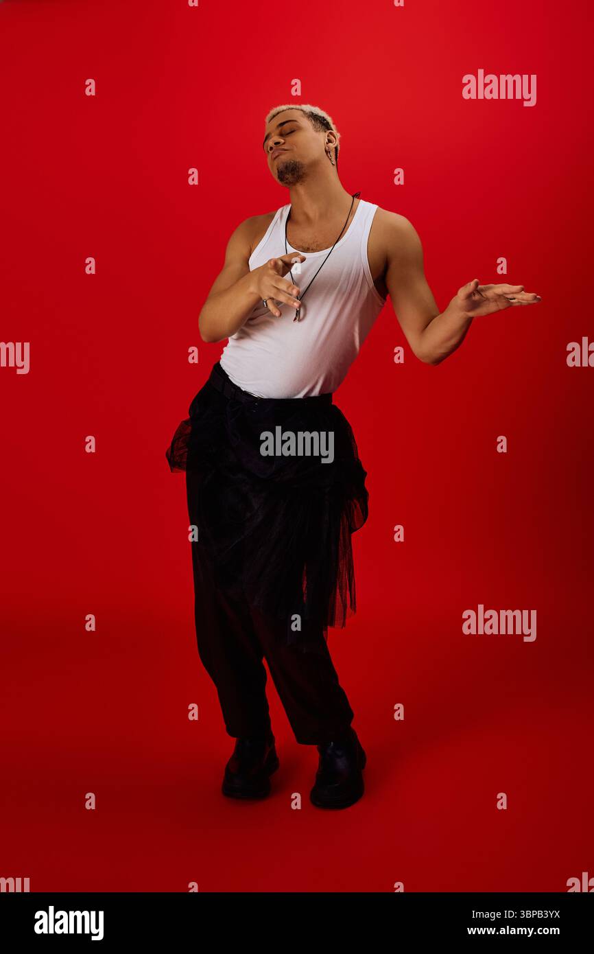 A young African American man strikes a stylish pose in a red studio ...