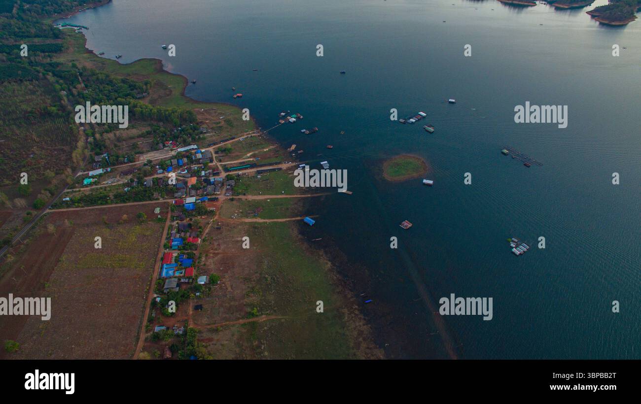 A breathtaking aerial view captures the soft glow of sunrise casting golden reflections over the tranquil waters of Vajiralongkorn Dam. Dotted with lu Stock Photo