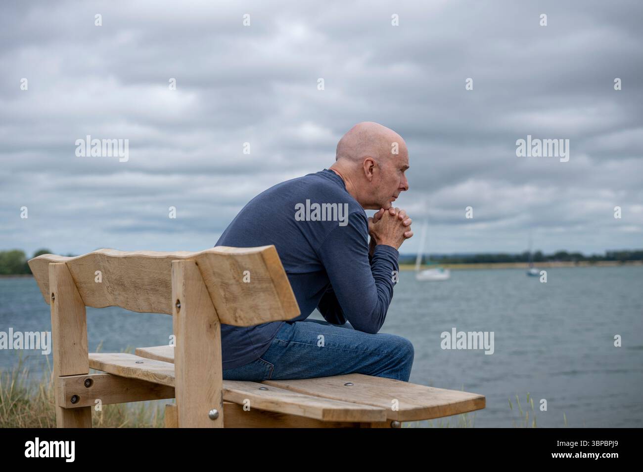 man sitting on a bench looking out to sea Stock Photo