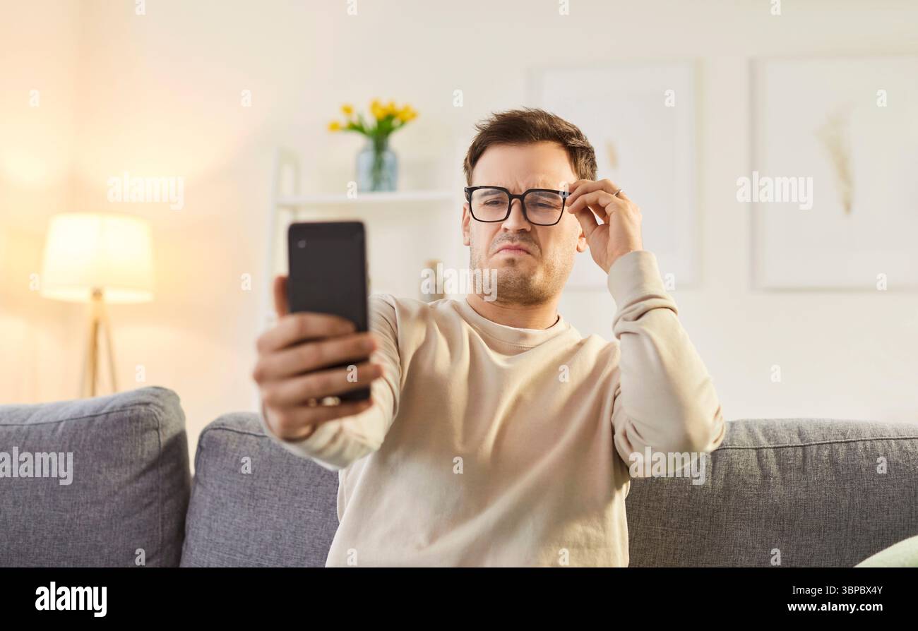 Discontent man focused in smartphone screen, looking through eyeglasses Stock Photo