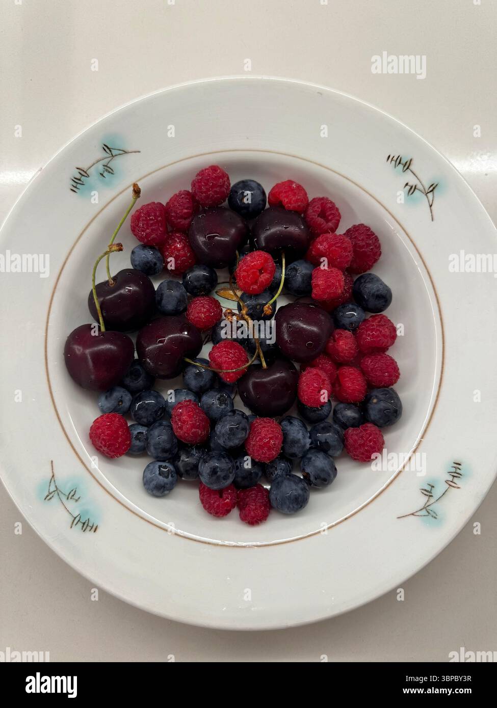 Cherry Vs Raspberry Size This image shows a top-down view of a white ceramic plate containing ...