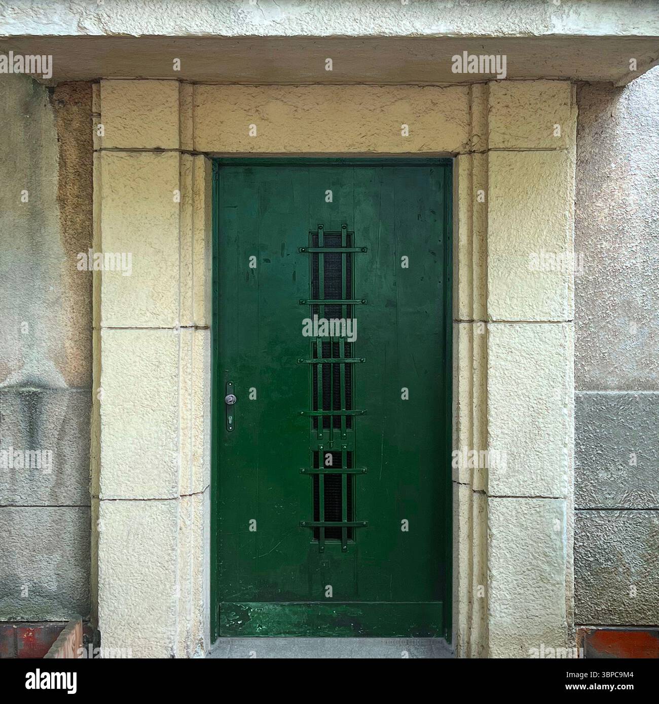 A minimalist green metal door with geometric grille detail, an example of 1930s modernist architecture in Warsaw - Smartphone Captured Stock Image