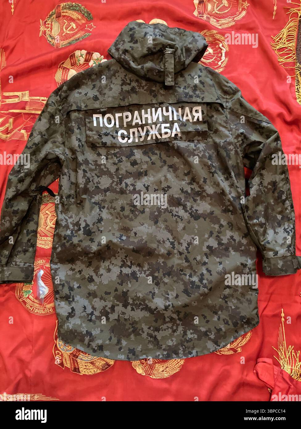 Russian Border Guard camouflage jacket with Cyrillic patch on Soviet banner background - Smartphone Captured Stock Image
