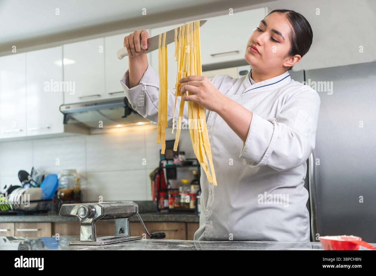 Chef preparing fresh pasta in a modern kitchen using a pasta machine Stock Photo