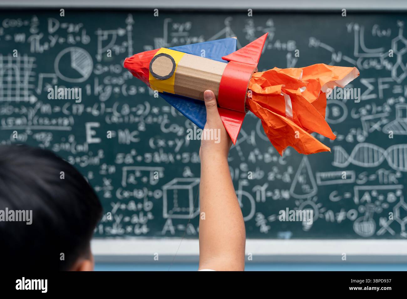 Student raising colorful handmade rocket craft in classroom, standing ...