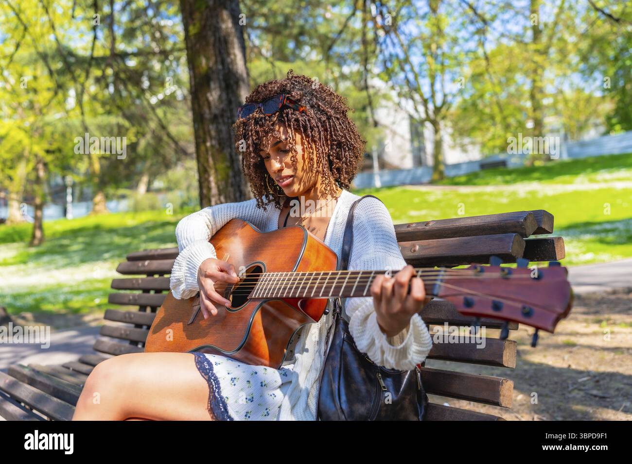 Curly haired woman sitting on a bench playing an acoustic guitar in a ...