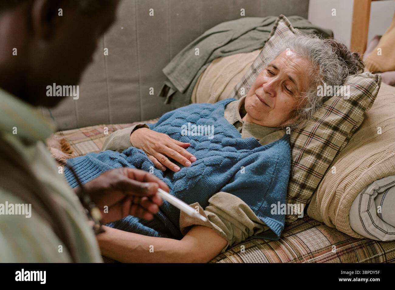 Senior Caucasian Woman Lying on Couch While Black Man Checking Temperature Stock Photo