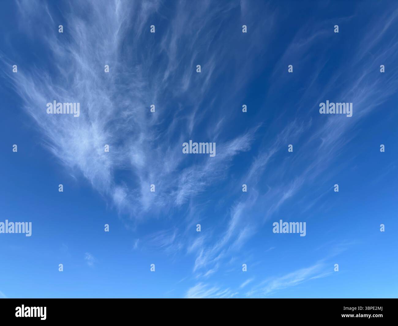 Beautiful wispy cirrus clouds drift across a vibrant blue sky on a sunny day. - Smartphone Captured Stock Image