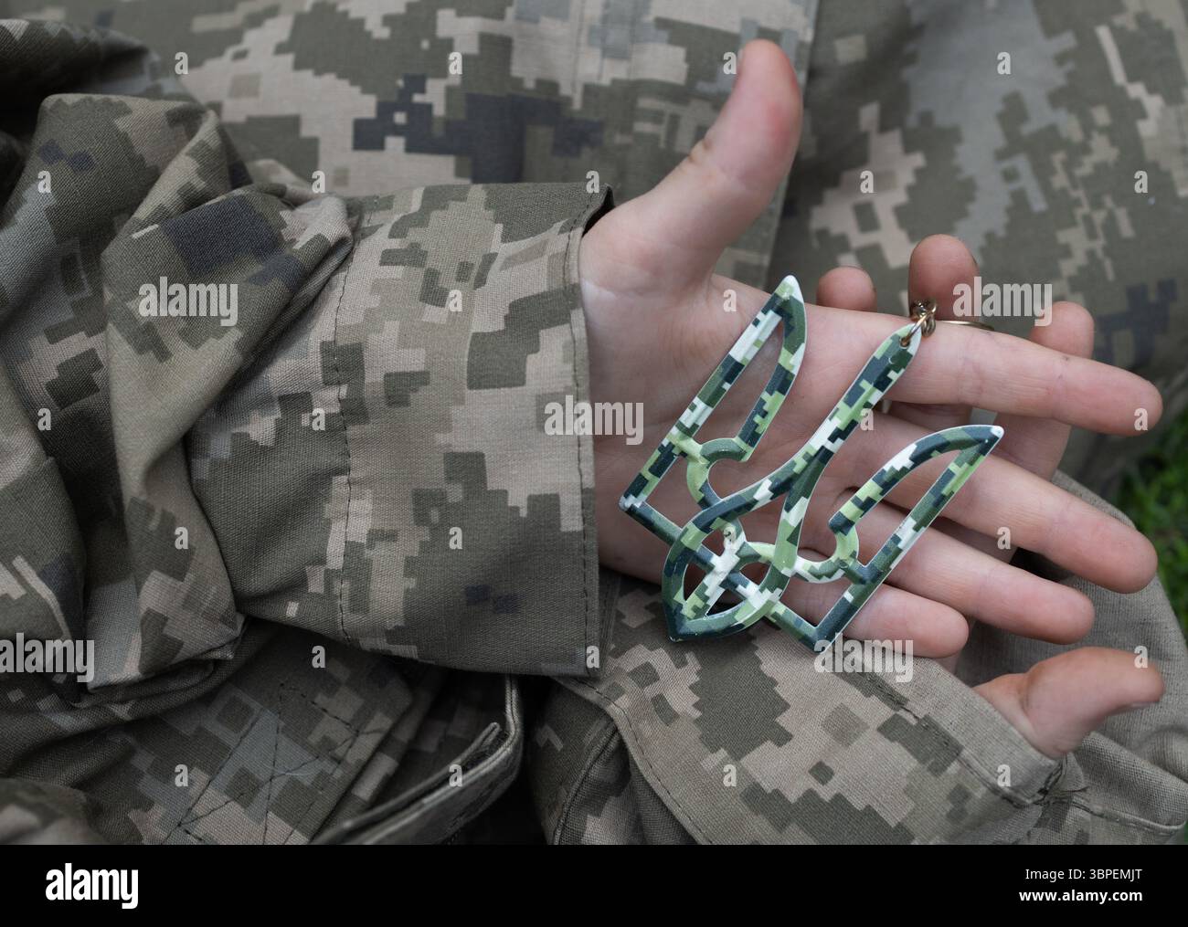hands in military pixel uniform holding trident - national symbol of ...